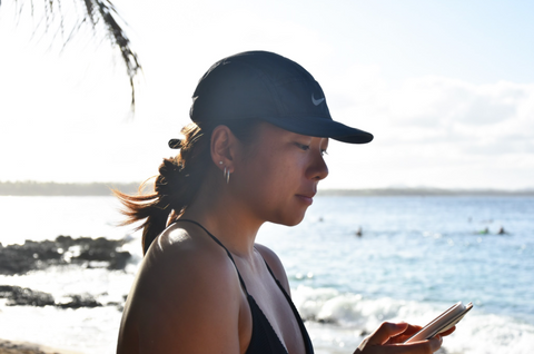 aziatisch meisje met nike-hoed op het strand kijkend naar telefoon surfen close-up profielfoto