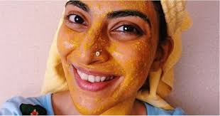 brown skinned woman with a yellow head covering smiles with yellow facial mask on her face.