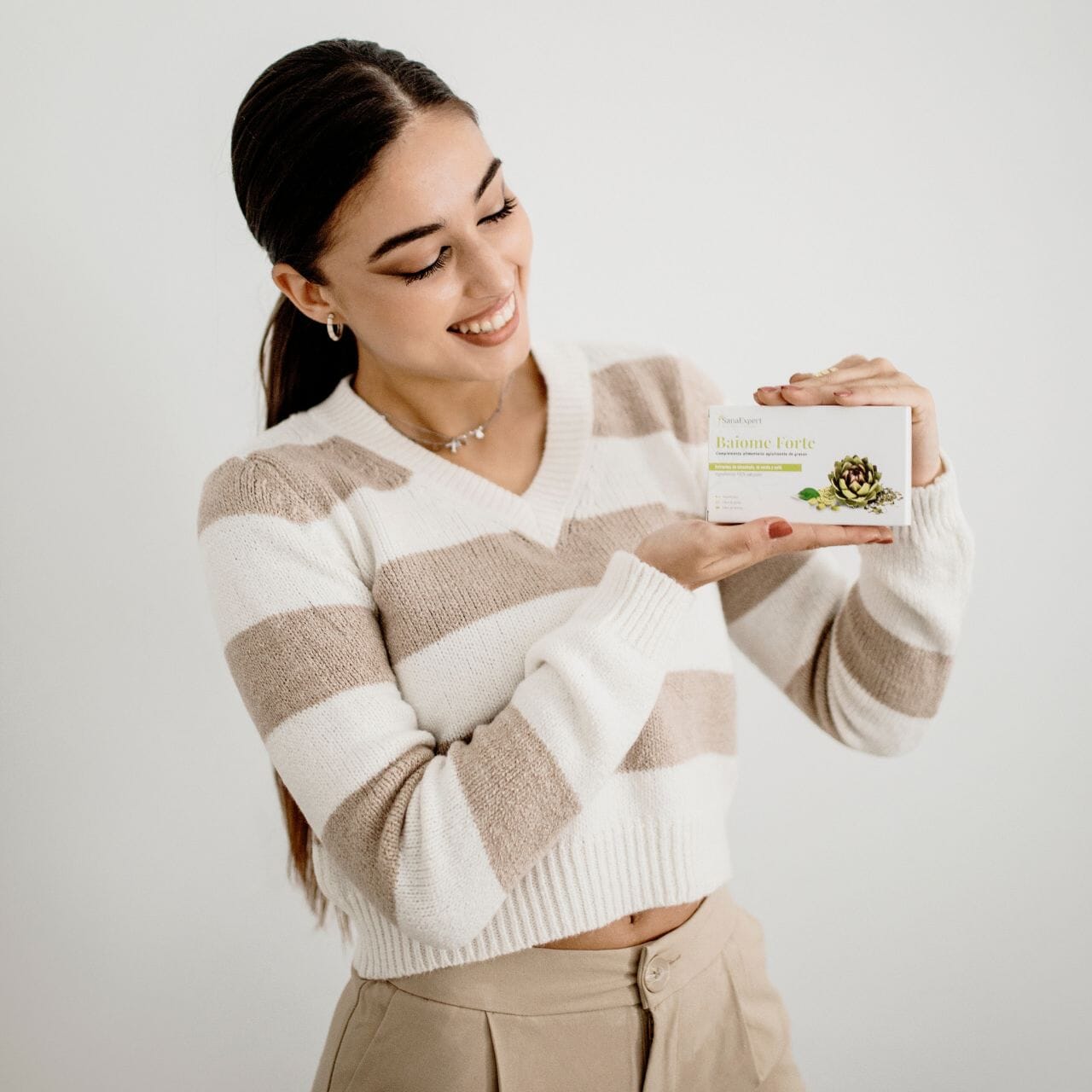Lächelnde Frau in einem gestreiften Pullover hält die Baiome Forte Verpackung in ihrer Hand, Produktpräsentation mit persönlichem Touch.