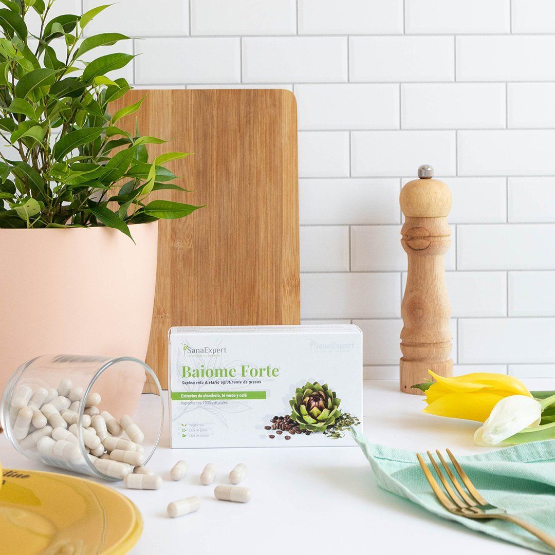  Baiome Forte Verpackung auf einem Tisch arrangiert mit gelber Tischdecke, Kapseln, Pfeffermühle und grüner Pflanze, Einladung zum gesunden Lebensstil.