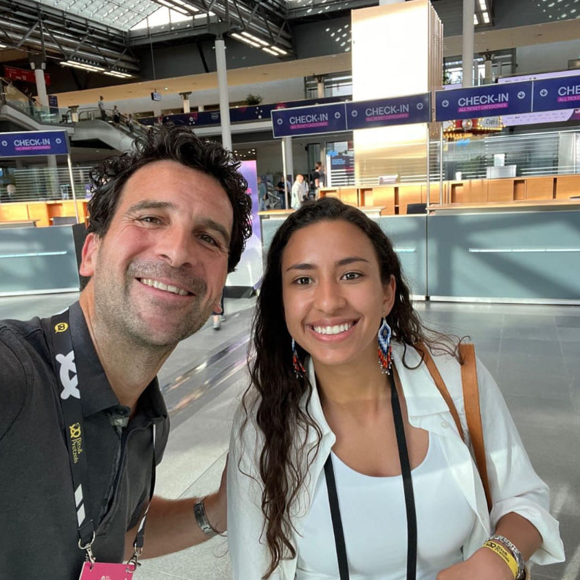 SanaExpert CEO Daniel und Business Developer Daniela machen ein Selfie im Flughafenterminal, mit leuchtenden Gesichtern und Check-in Schaltern im Hintergrund.