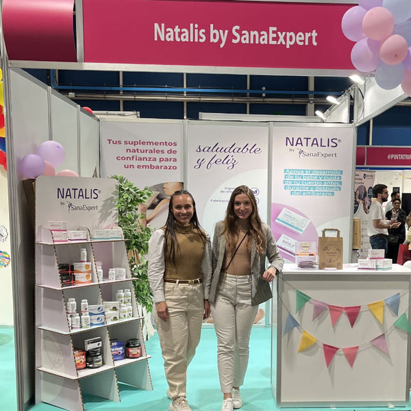 Lina und Laura von SanaExpert stehen vor einem farbenfrohen Natalis-Messestand, umgeben von Produktdisplays und fröhlicher Dekoration.