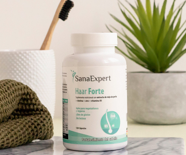 Eine Flasche SanaExpert Haar Forte steht auf einer hellen Oberfläche neben einer Zahnbürste aus Bambus und einer grünen Zimmerpflanze.