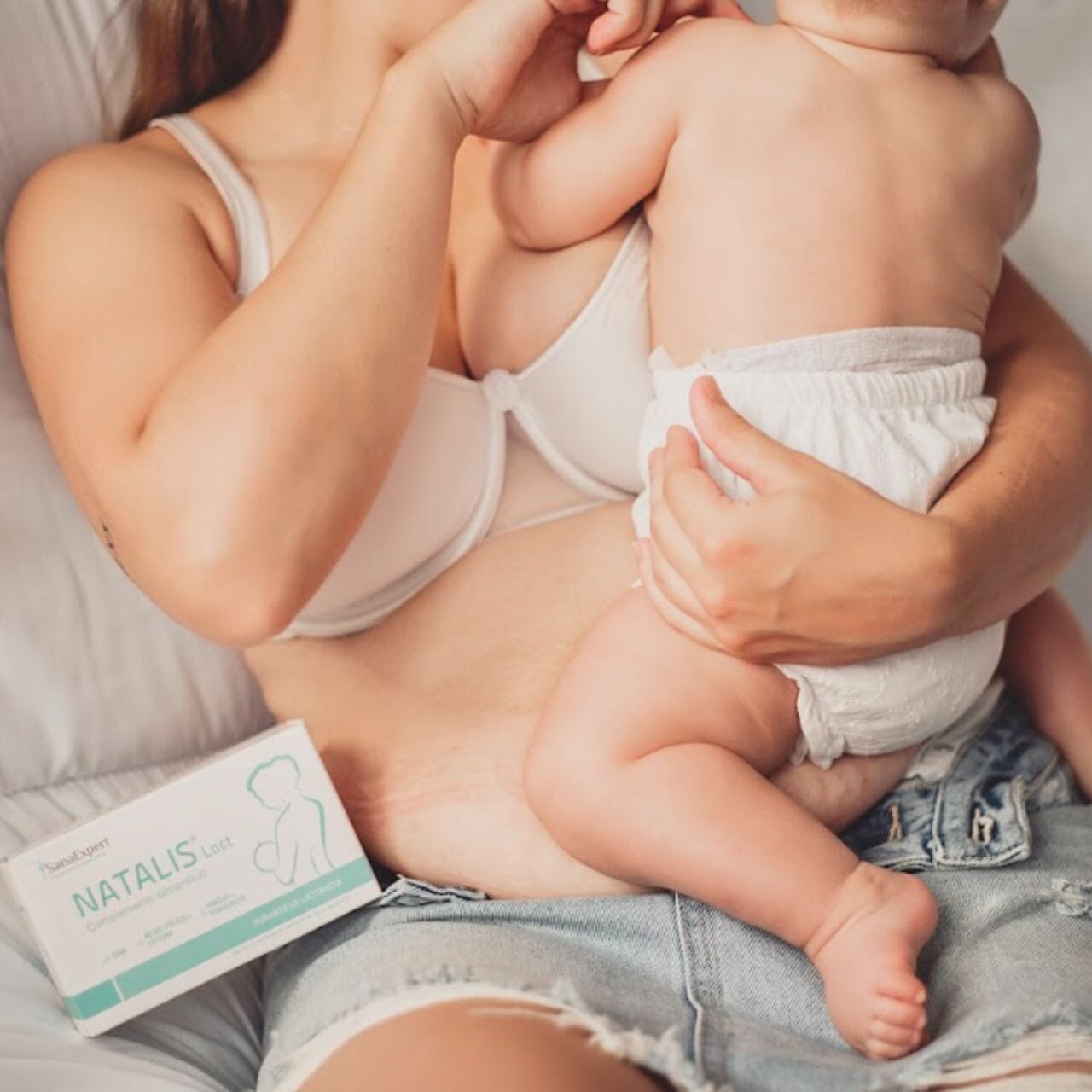 Junge Mutter beim Stillen ihres Babys, neben ihr eine Packung Natalis Lact auf dem Schoß.
