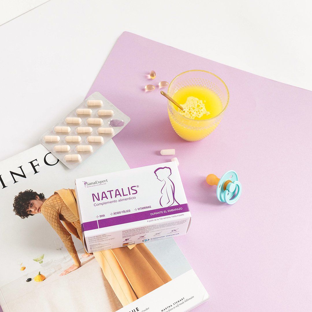  Natalis Box neben einem Glas Orangensaft und Babyschnuller auf einem pastellfarbenen Hintergrund, morgendliche Stimmung.