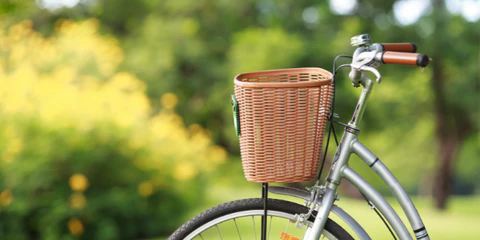 Ein einsames silbernes Fahrrad mit einem Korb, abgestellt im sonnigen Park mit gelben Blumen im Hintergrund.