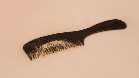 Eine Nahaufnahme eines schwarzen Kamms, der mit verlorenen hellblonden Haaren gefüllt ist, auf einem blassen Hintergrund.