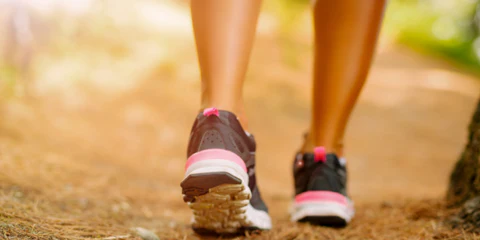 Nahaufnahme der Füße einer Joggerin in Sportschuhen, die auf einem Waldweg läuft, umgeben von grüner Natur.