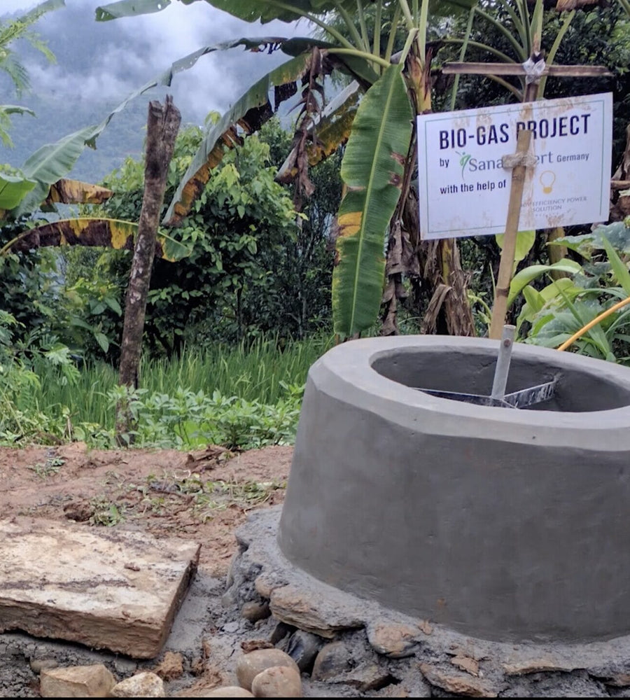 Biogas-Anlage im Freien mit einem Schild, das das Biogas-Projekt von SanaExpert ankündigt, umgeben von tropischer Vegetation.