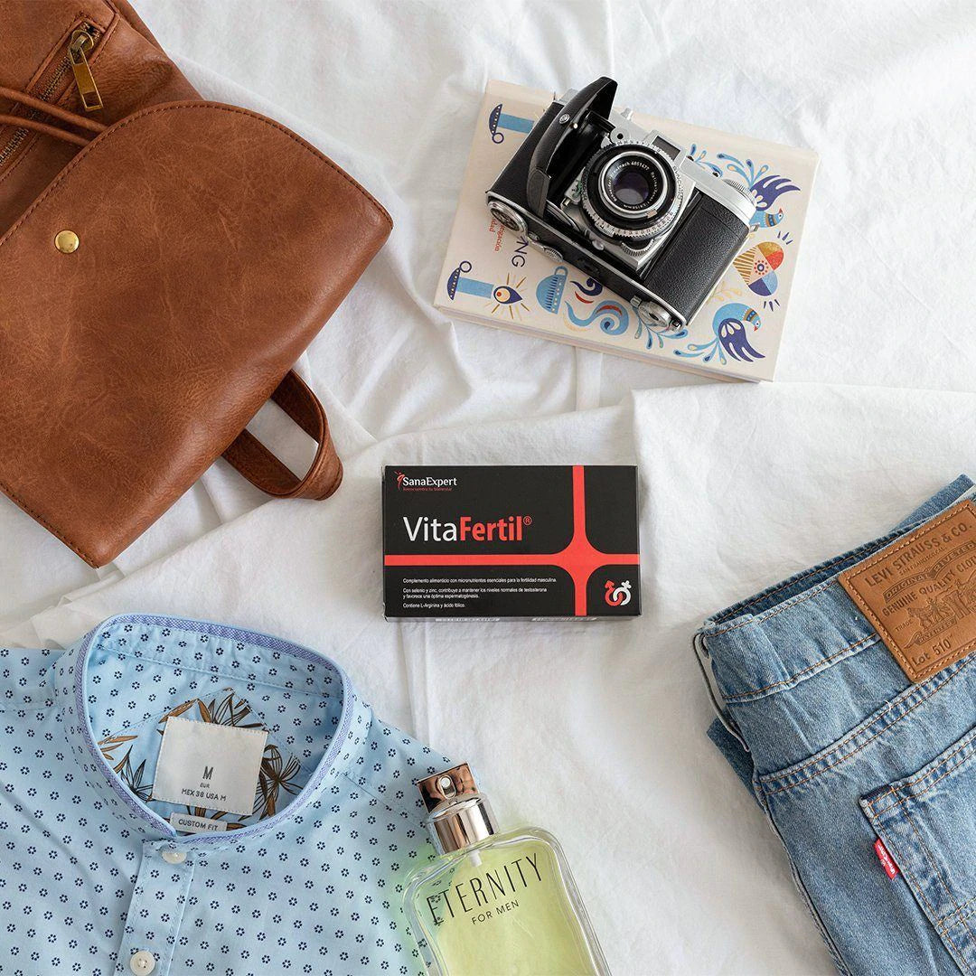 Eine Packung VitaFertile auf einem Bett neben einer braunen Tasche, einer Kamera und einer Jeans, Alltagsgegenstände im Hintergrund.