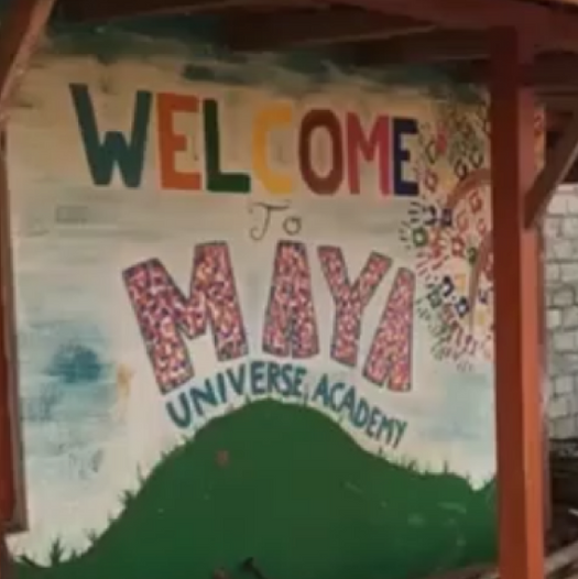 Ein handgemaltes Begrüßungsschild mit der Aufschrift "Welcome to MAYA Universe Academy" in bunten Farben und Kindershandschuh-Drucken als Dekoration.