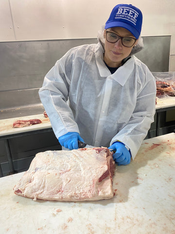 Rancher Sarah in wearing personal protective equipment as she cuts up an uncooked beef standing rib roast.