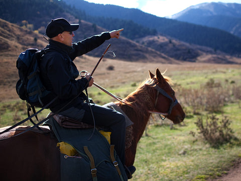 man riding horse through the mountains pointing at something in the distance