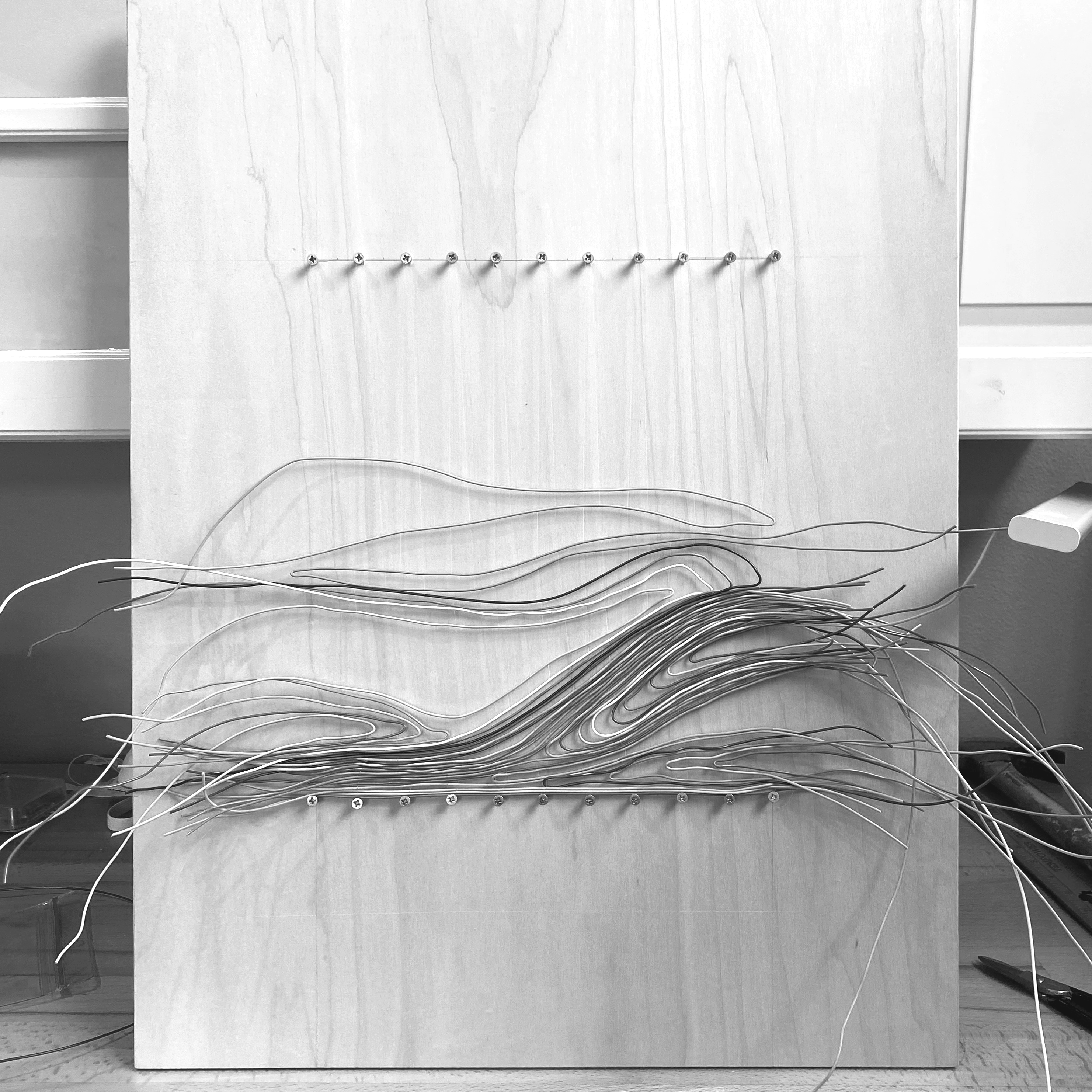 A process image of a wire weaving on a wood board with the wires going in all directions before getting trimmed