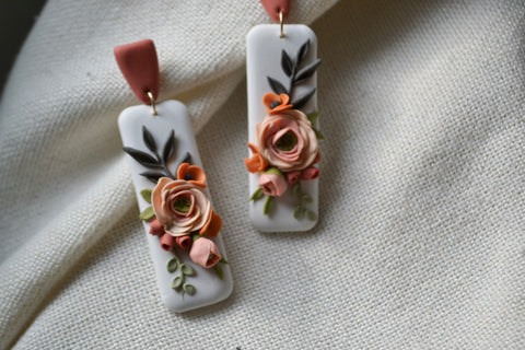 white rectangle dangle earrings with a terra cotta top stud and floral design on a brightly lit cream background