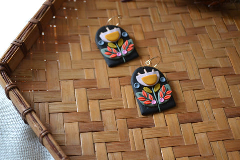 a pair of arch-shaped black earrings with colorful folk flower design on a woven basket background