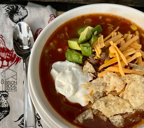 Bison taco soup with avocado, cheese, sour cream and crushed tortilla chips