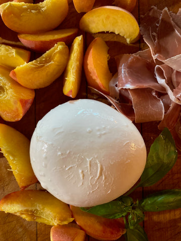 Burrata surrounded by sliced peaches, basil and proscuitto