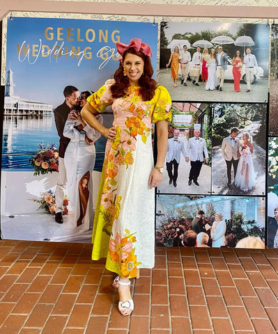 Jessie is wearing a yellow dress with pink bow headband standing in front of a wedding buildboard