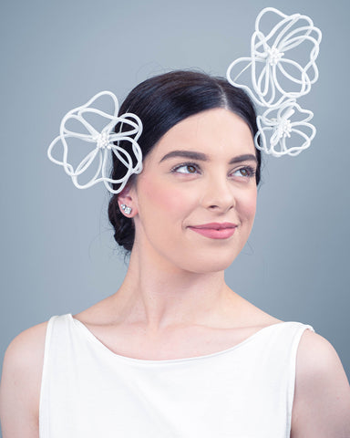 A dark haired model is wearing a headpiece that is made up of three floating white wire flowers