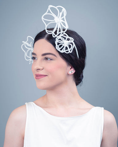 A dark haired model is wearing a headpiece that is made up of three floating white wire flowers