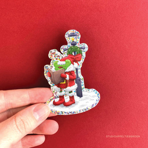 Hand holding up a glitter vinyl sticker of a frog singing christmas carols