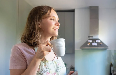 woman drinking tea from a cup and looking out the window in the kitchen