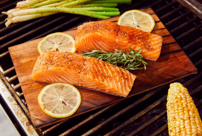 2 salmon fillets being grilled on a cedar plank with Auntie Nono's Seafood Seasoning and lemon slices 