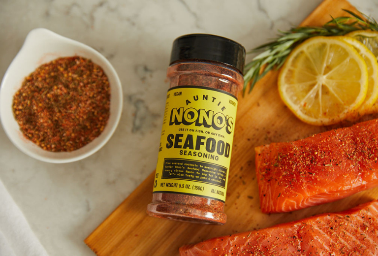 auntie nono's seafood seasoning on a wooden cutting board with salmon and lemon slices 