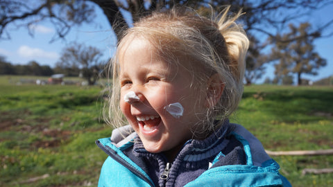 Laughing girl with lotion on nose and cheeks.