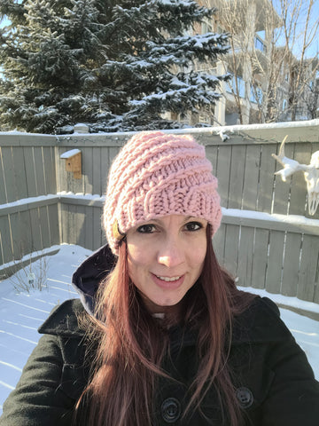 Photo showing a woman, Mel, in the snow wearing a pink beanie made with Stitch & Story The Chunky Wool.