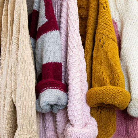 Image showing 5 knitted sweaters hung up with some sleeves folded up. Featuring Avalon cardigan, roma striped sweater, atlantis cable sweater, verona lace cardigan and stefano sweater.