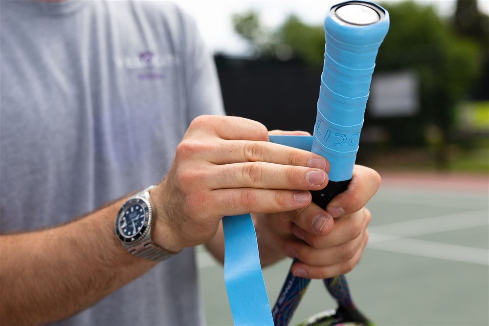 Hands applying a tennis racquet overgrip
