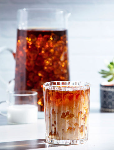 Glass of iced coffee with cream in front of a pitcher of coffee. 