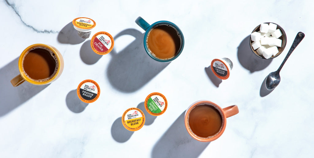 Variety of OneCUP pods on table with coffee cups.