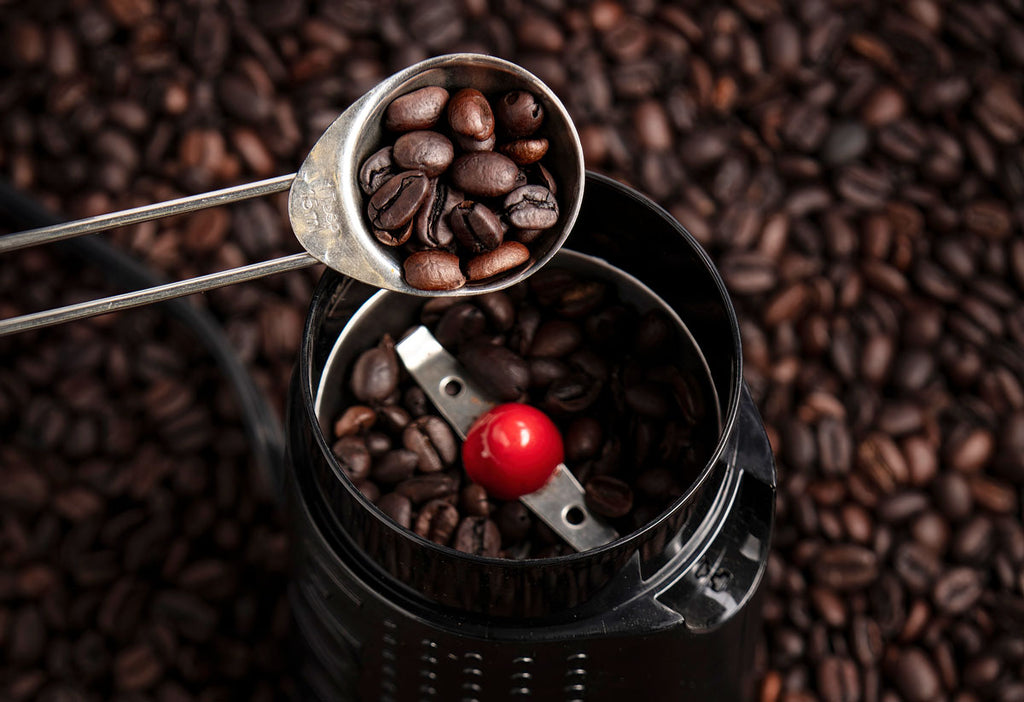 Tablespoon of coffee beans going in grinder.