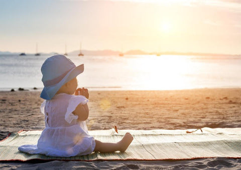 Baby with large rimmed hat in the evening sun on the beach.