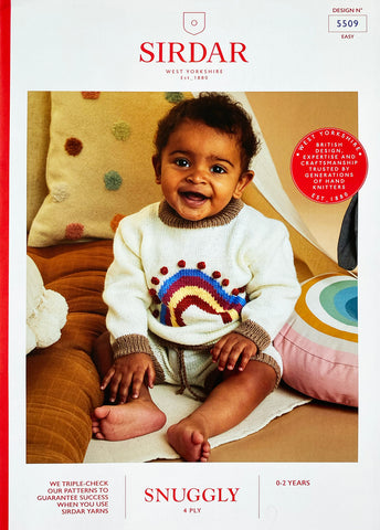 Image of cover of Sirdar knitting pattern showing a young baby wearing a sweater and shorts knitted set featuring a rainbow with pom pom detail on the front