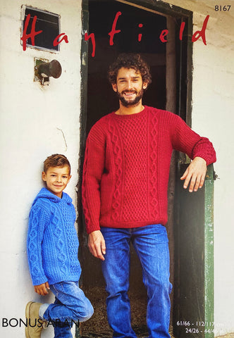 Image of cover of Sirdar knitting pattern 8167 showing an Aran sweater with a round neck hand knitted in red and modelled by a man, and a hooded version in light blue modelled by a young boy