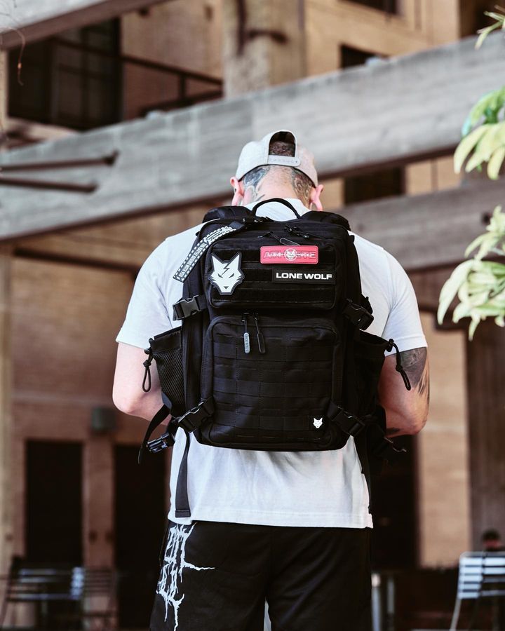 Man wearing a black backpack walking outside of an office building 