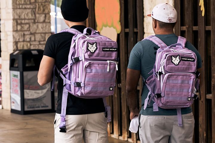 Two men wearing matching lavender fitness backpacks walking outside of a shop