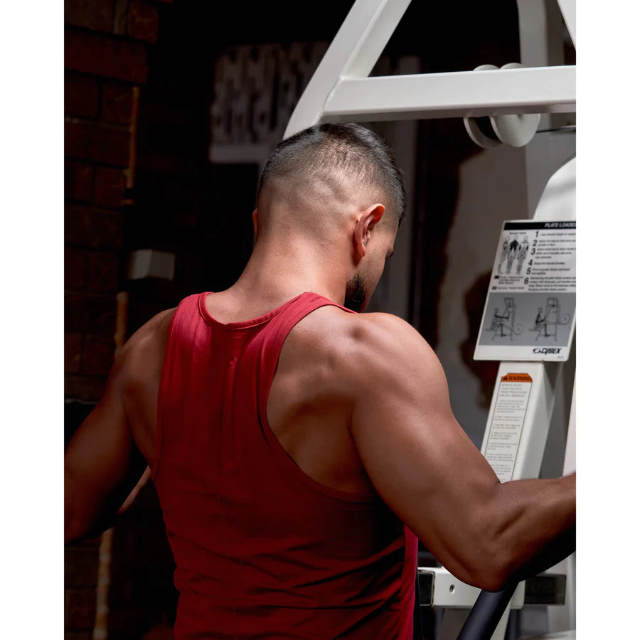 The back of a man working out his arms at the gym in a red men’s drop cut tank top.