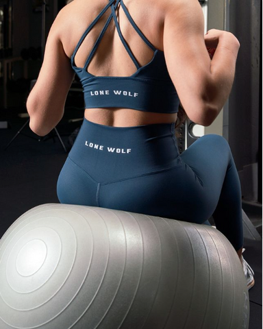 Woman wearing blue premium women’s workout leggings and sports bra, sitting on a workout ball