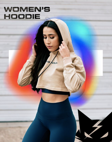 Woman wearing a tan athletic crop top jacket and blue leggings as an athleisure outfit with a colorful background and Lone Wolf Fitness logo in the bottom corner