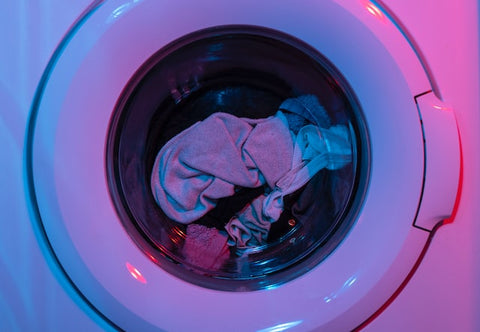  Gym clothes in a white washing machine with red and blue light reflecting on the machine