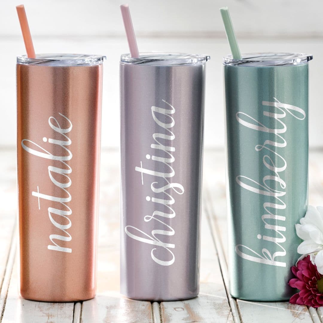 Three drink tumblers on a table, each with names and straws