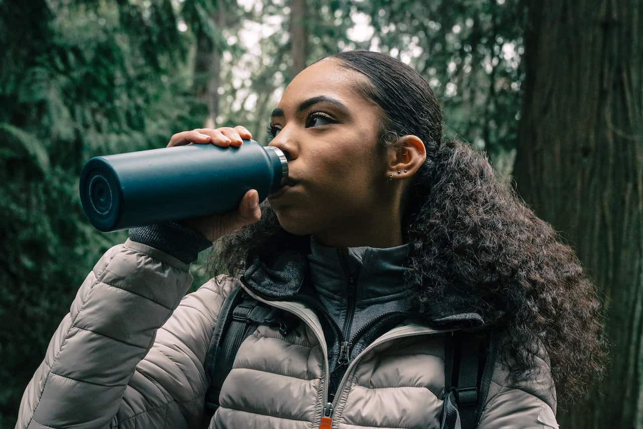 A woman drinks out of a reusable water bottle in the forest