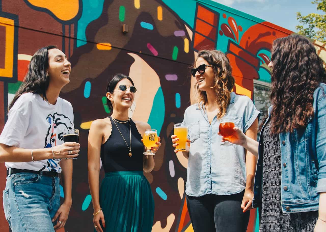 Women standing in front of mural with drinks