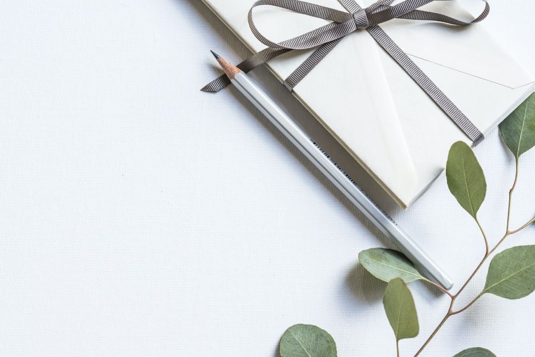 An envelope with a bow next to a pencil and branch.