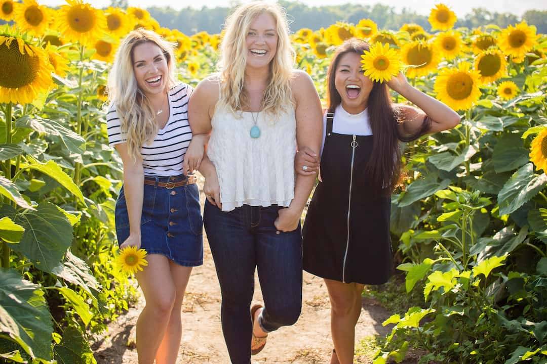 Three women smiling in a sunflower field